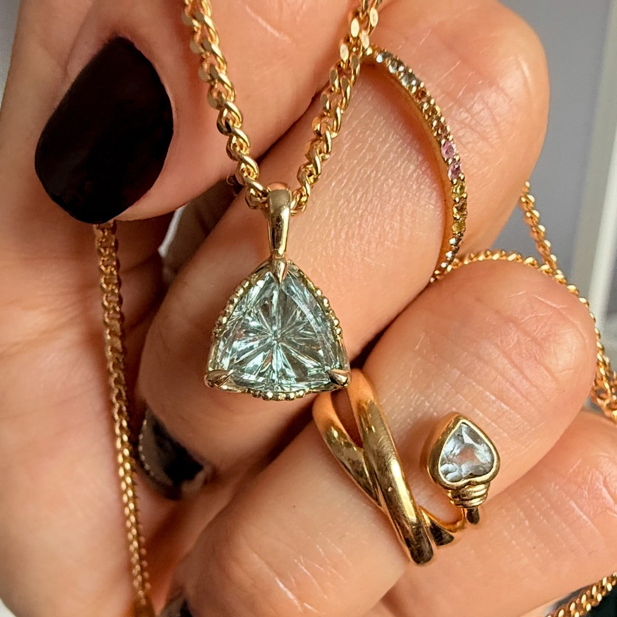 Gold necklace and ring with a heart-shaped gemstone held in a hand.