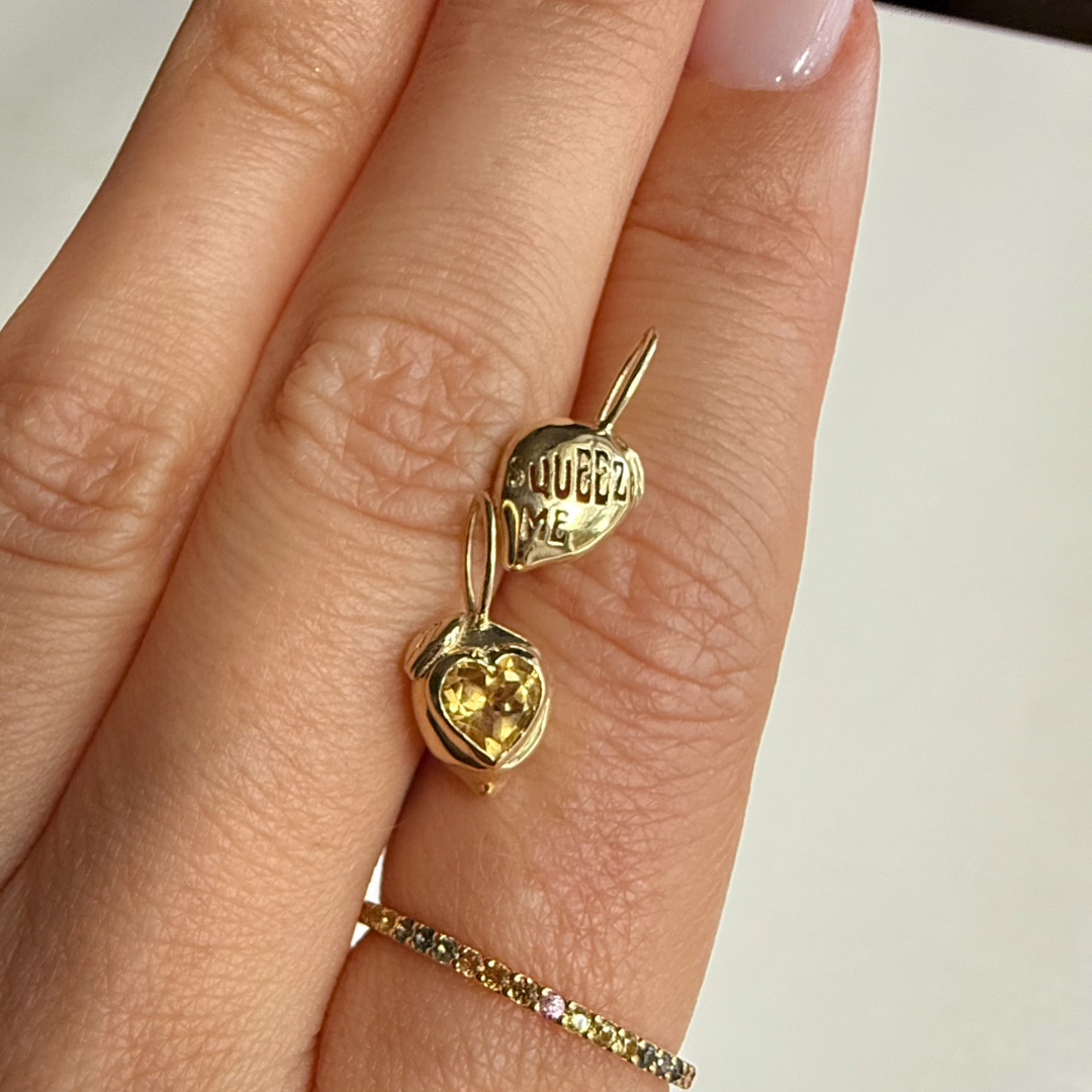 Gold rainbow pave ring with two lemon shaped pendants on a hand against a white background
