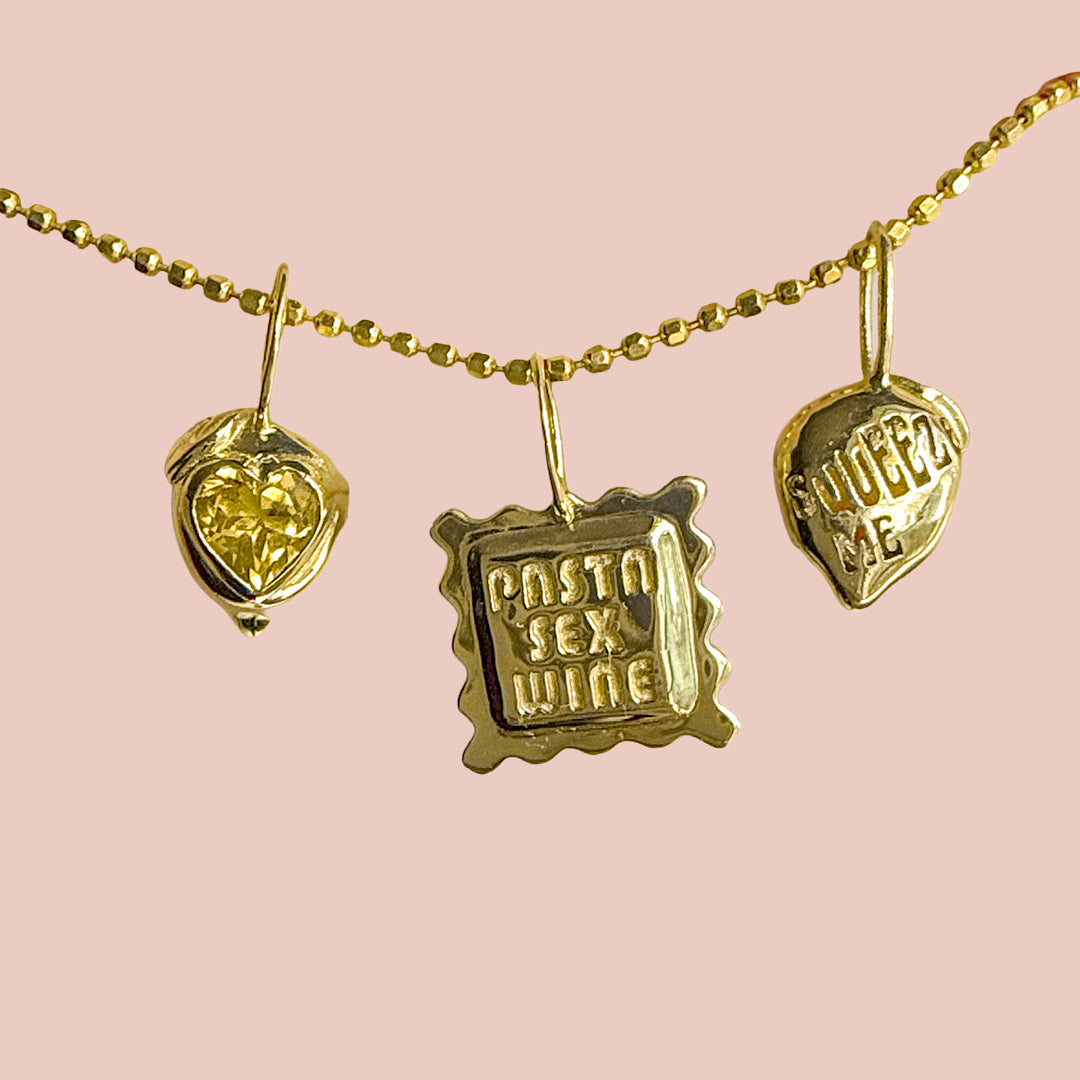 Gold necklace with three pendant charms on a pink background