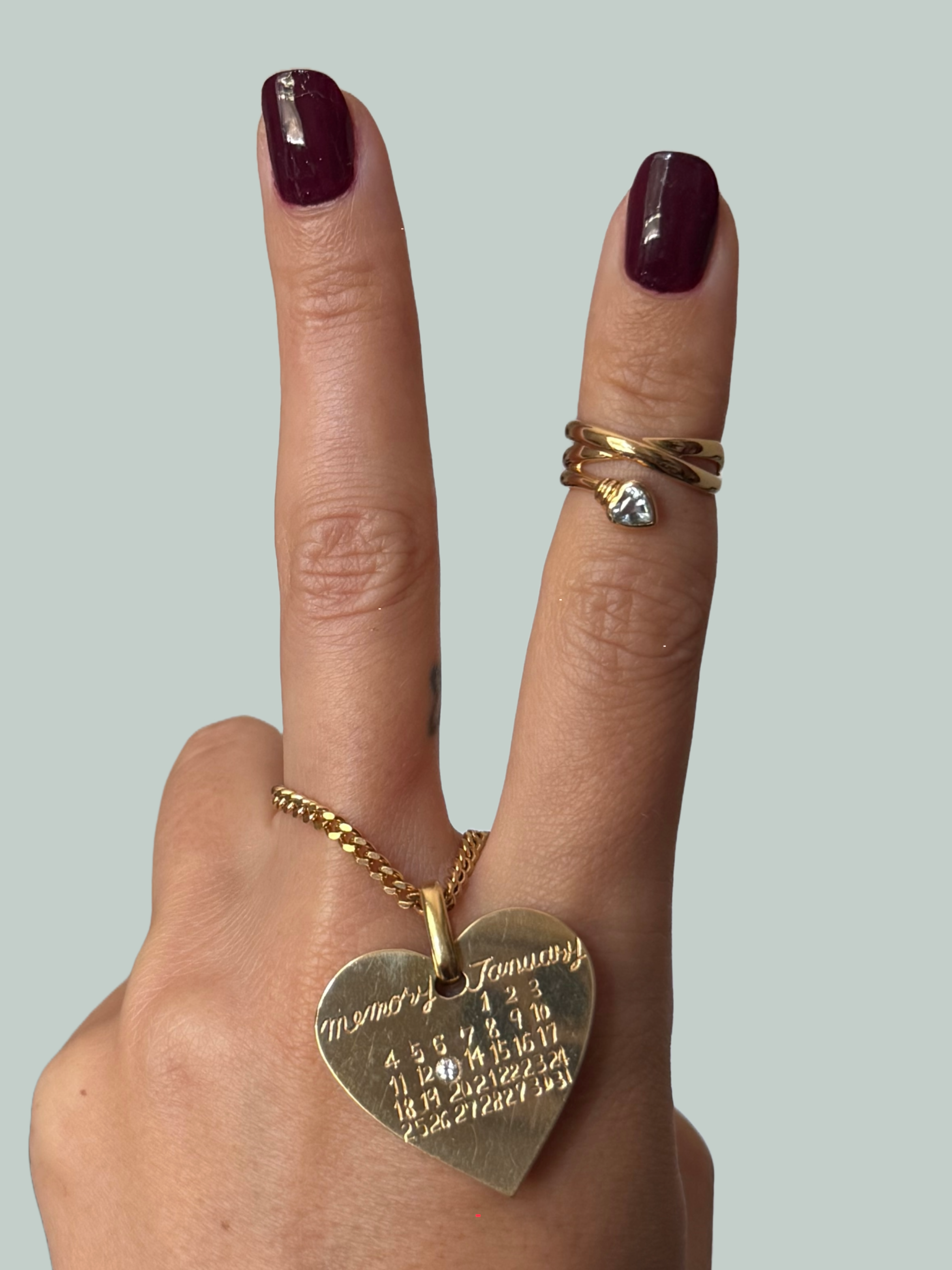 Hand making a peace sign with gold rings on fingers against a gray background