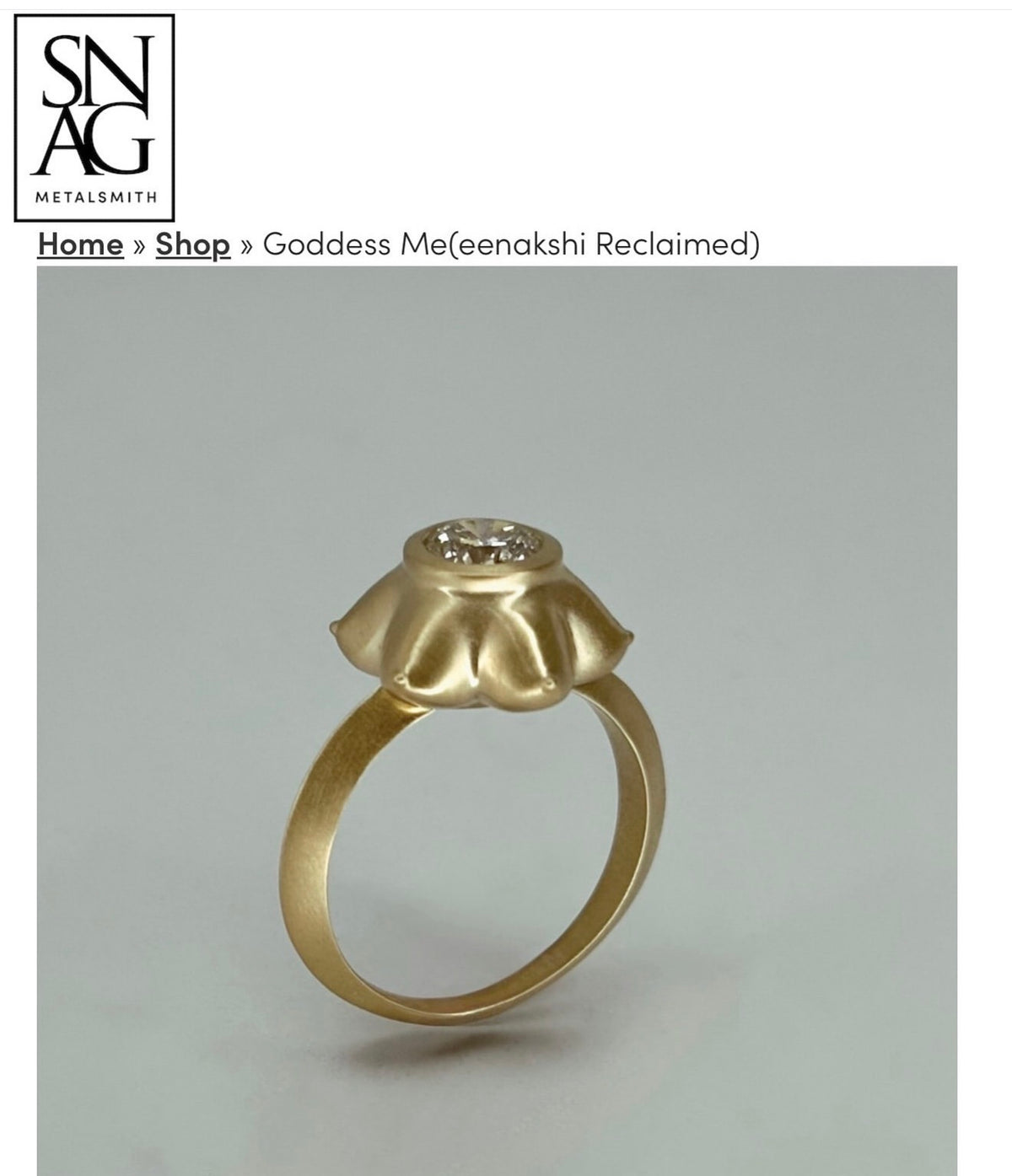 Gold ring with a diamond on a gray background, featuring the brand 'SNAG Metalsmith'.
