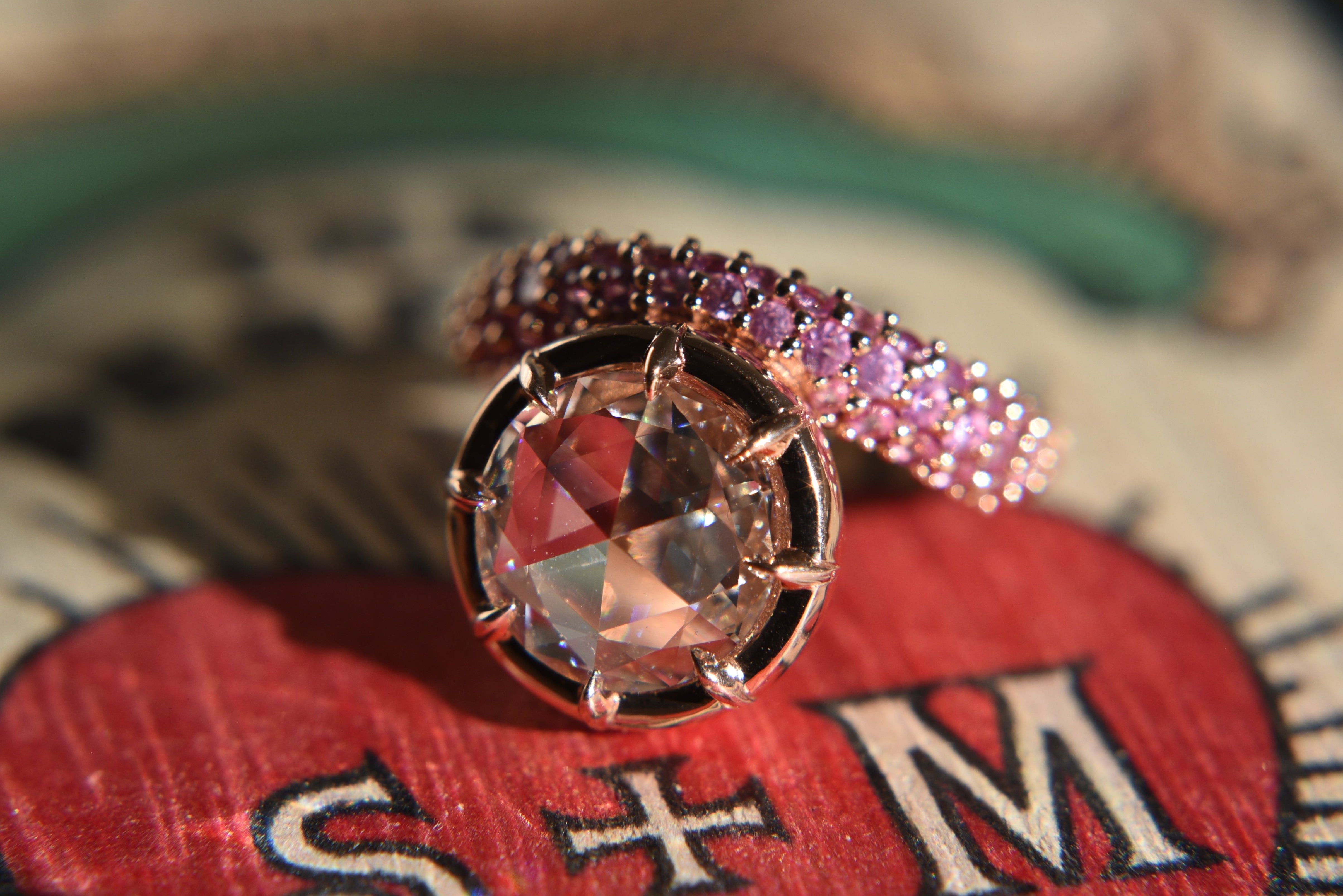 Close-up of a rose cut diamond ring with claw prong setting on an asymmetrical wavy pink sapphire gold band.