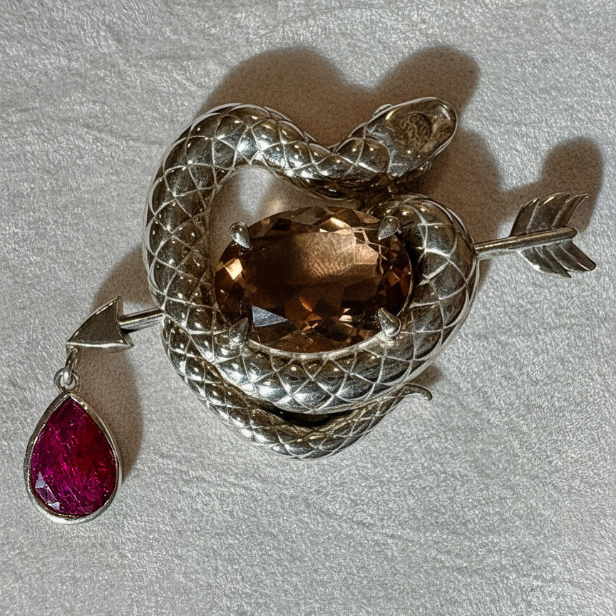 Silver snake brooch with brown quartz and ruby gemstone on a light grey background