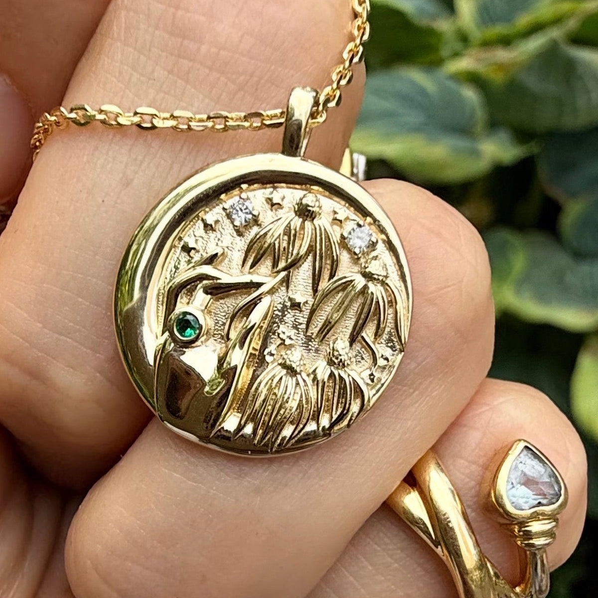  14k gold coin pendant with hand gathering coneflowers, diamonds and emerald, held in hand
